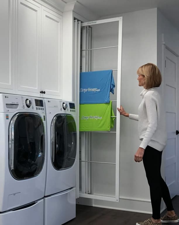 Woman pulling out an extended DryAway drying rack beside a washer and dryer, with a blue and green towel hanging on the rods
