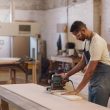 Carpenter man and sanding machine in workshop with woodwork project furniture production and craft Artisan person and manufacturing with glasses electric tools or carpentry equipment for timber