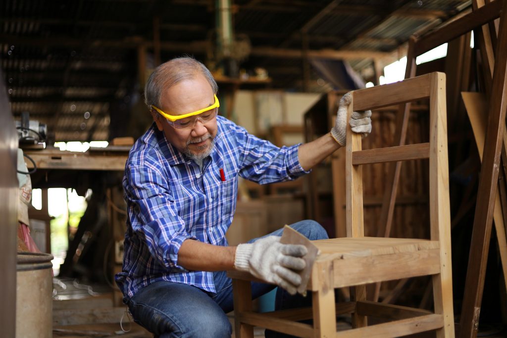 Senior Asian carpenter man is repairing wooden chair in his own garage style workshop at retirement age for hobby with copy space - Wurth Louis and Company Senior Asian carpenter man is repairing wooden chair in his own garage style workshop at retirement age for hobby with copy space